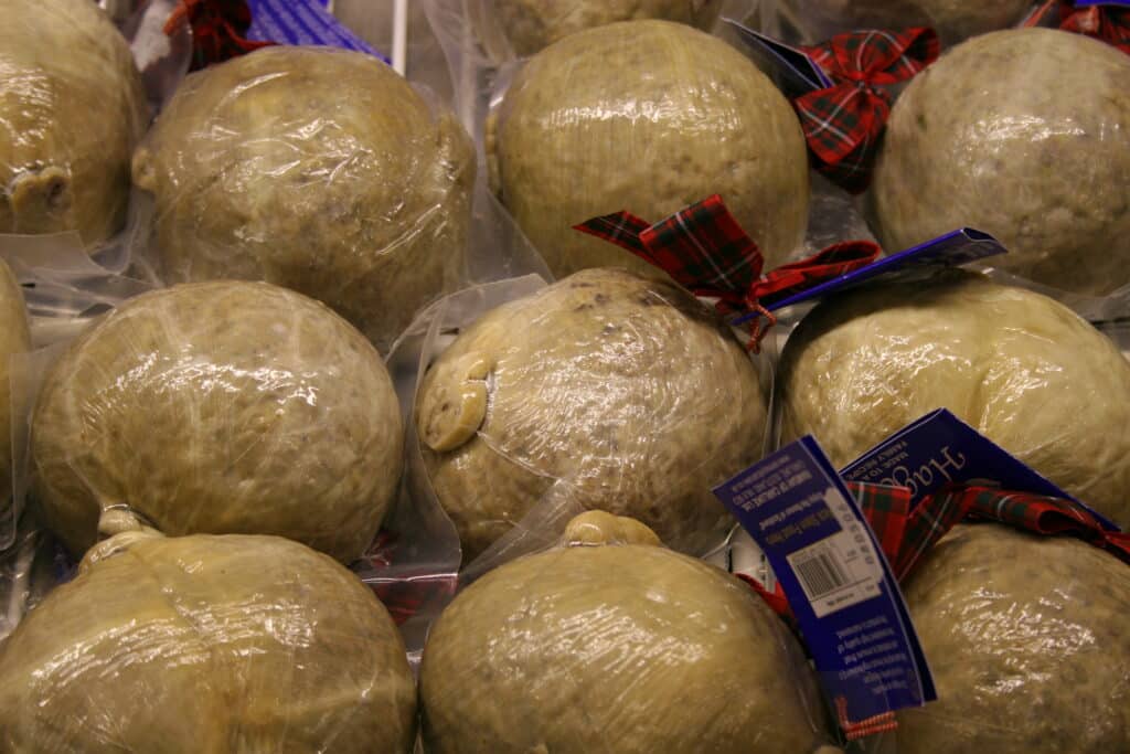 Stacks of round cheese wheels wrapped in plastic with red plaid ribbons and blue product tags.