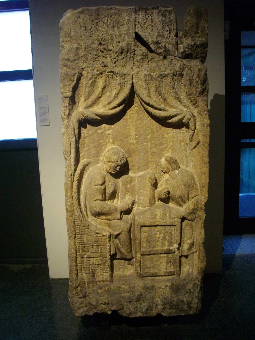 Gallo-Roman limestone stele showing two seated figures at a table, read as a payment of taxes
