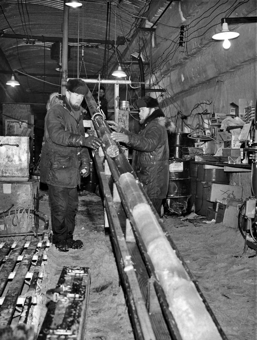 Engineers handling a long cylindrical ice core inside a snow tunnel at Camp Century, Greenland