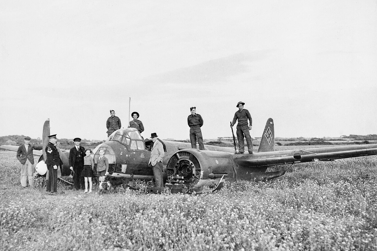 Troops and civilians gathered around a large German bomber lying in a field