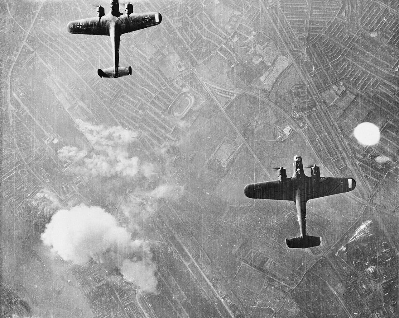 Two twin-engined bombers seen from above against a landscape streaked with smoke