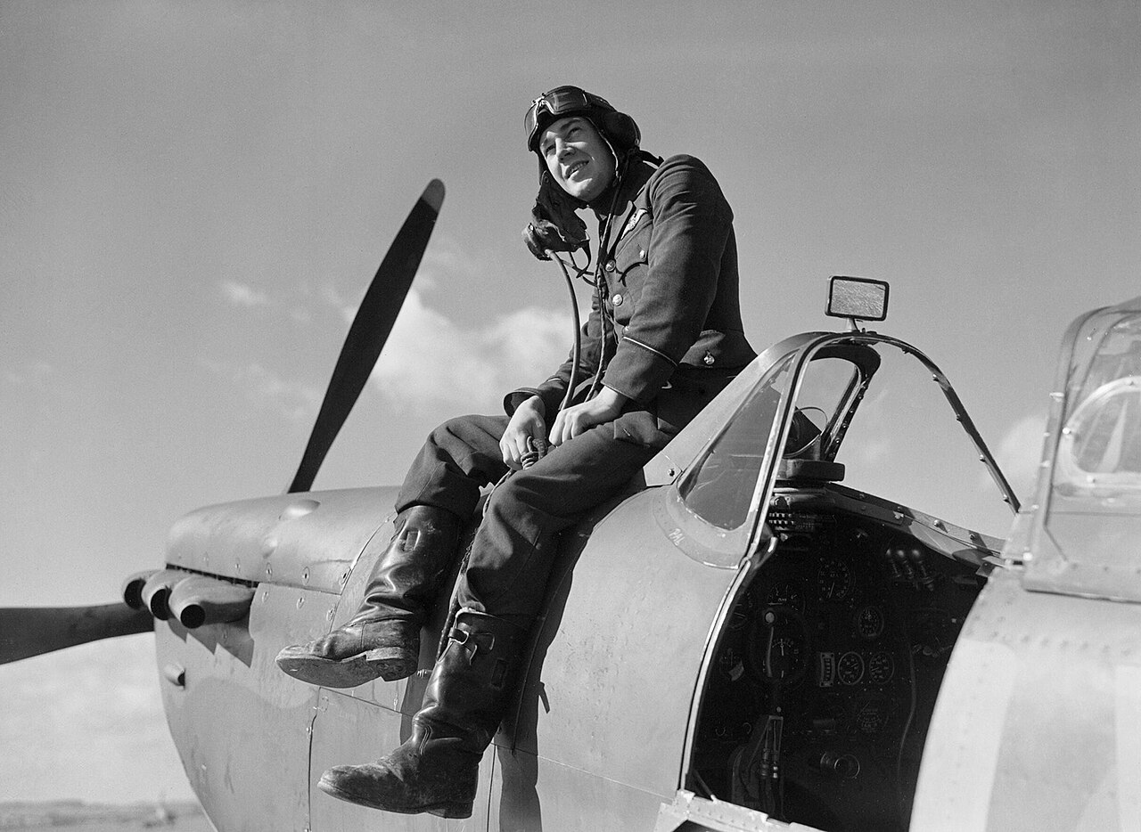 A young pilot sitting on the cockpit sill of a Spitfire, looking towards the camera