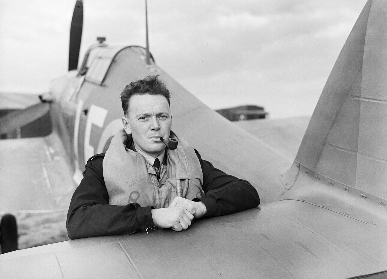 A pilot leaning on the tailplane of a Hurricane, still in flying kit