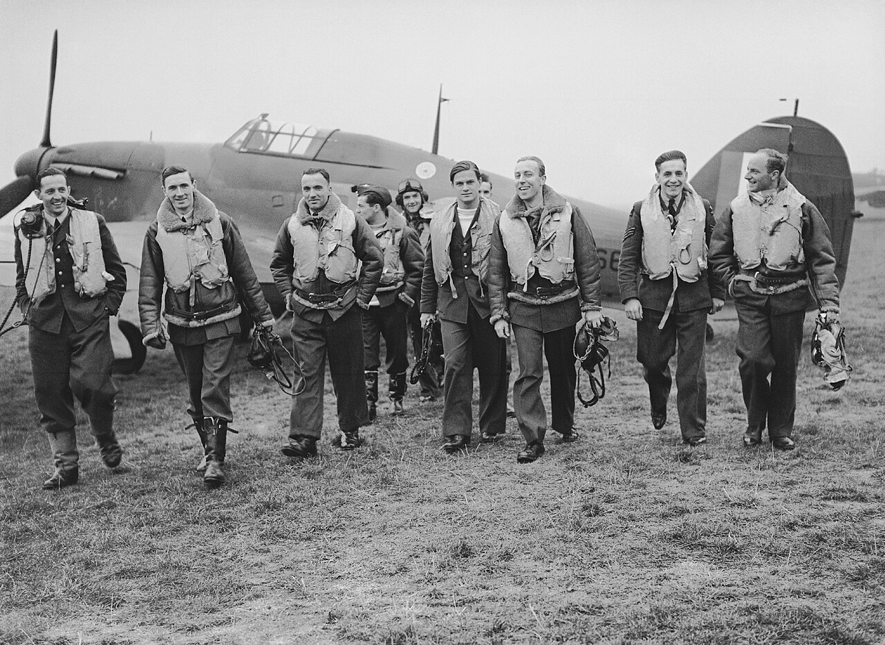 A group of pilots walking together in front of a Hurricane on an airfield
