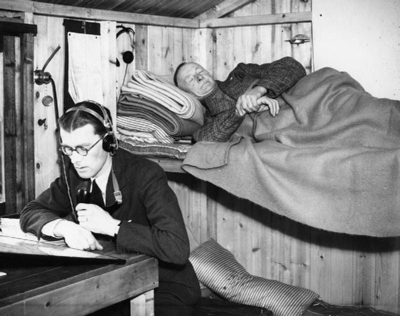 One man listening for aircraft at an observation post while a second sleeps beside him