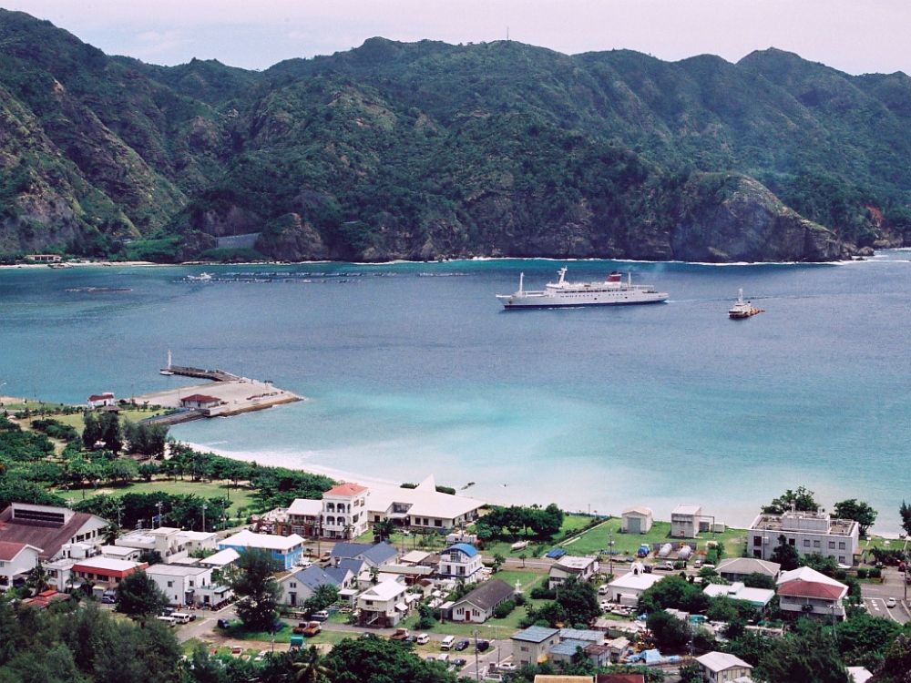 Futami harbor on Chichijima, a sheltered turquoise bay ringed by steep, forested mountains, with a small town along the shore