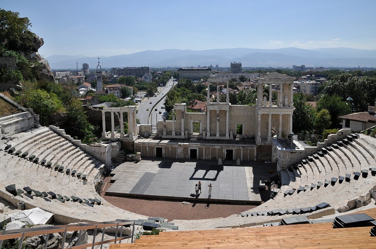 The restored Roman theatre of Philippopolis in modern Plovdiv, Bulgaria, its stone seating curving around a stage building with columns, the modern city beyond