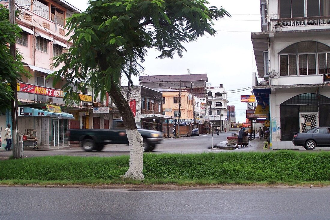A street in Georgetown, Guyana, with shopfronts, awnings and a pickup truck passing a grass verge
