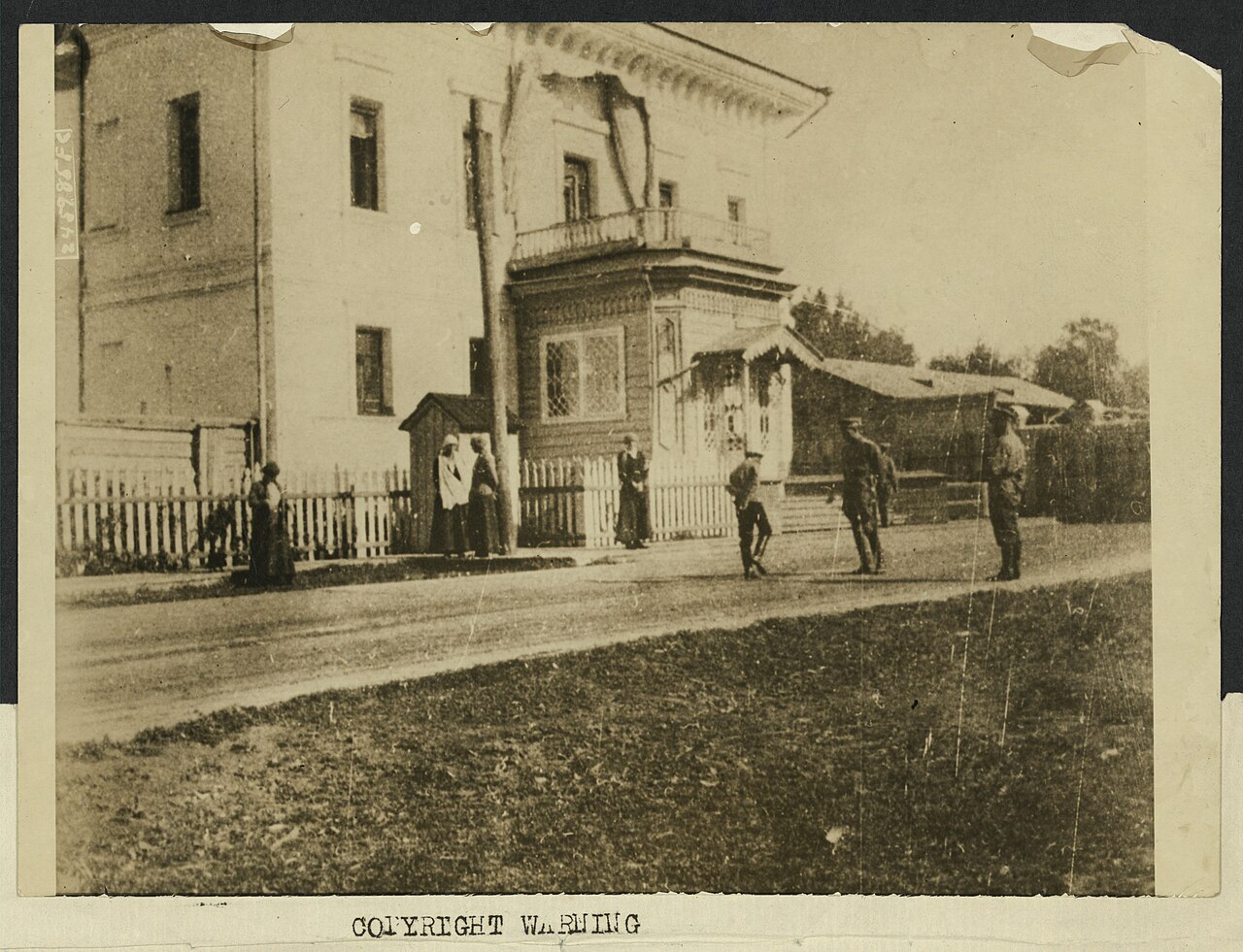 Figures standing on the street before the main entrance of a large house