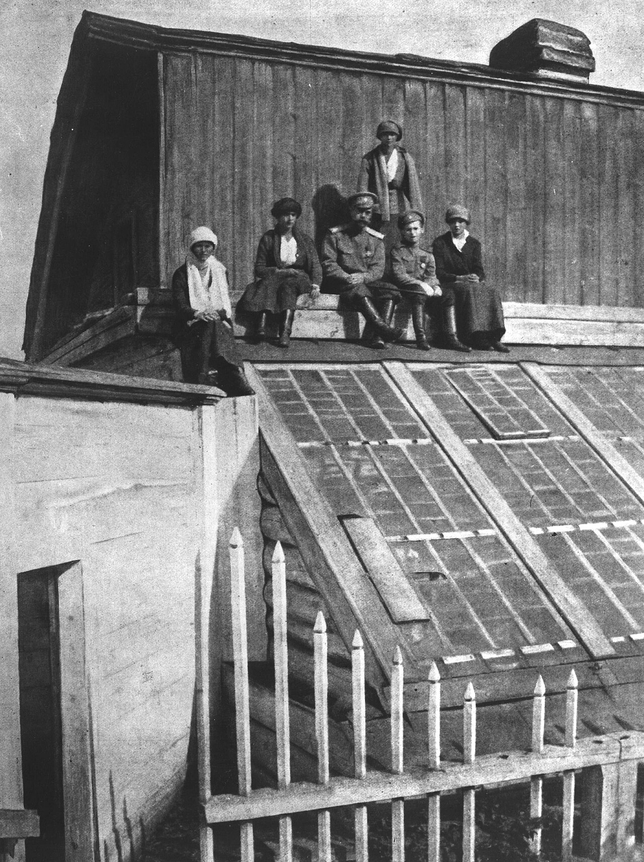 Several figures sitting in a row along the ridge of a glasshouse roof