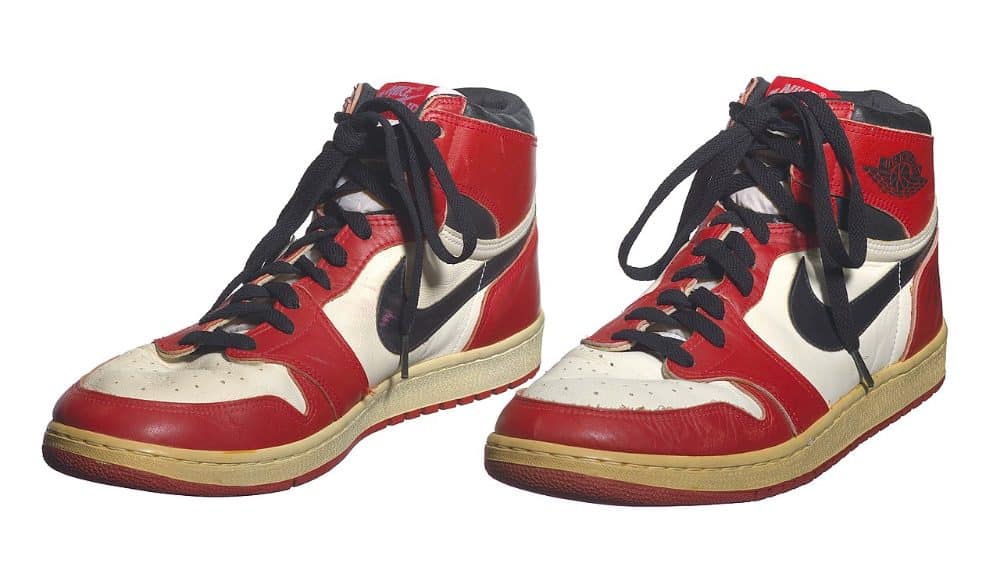 A pair of worn red, white and black high-top 1985 Air Jordan 1 sneakers photographed against a white background