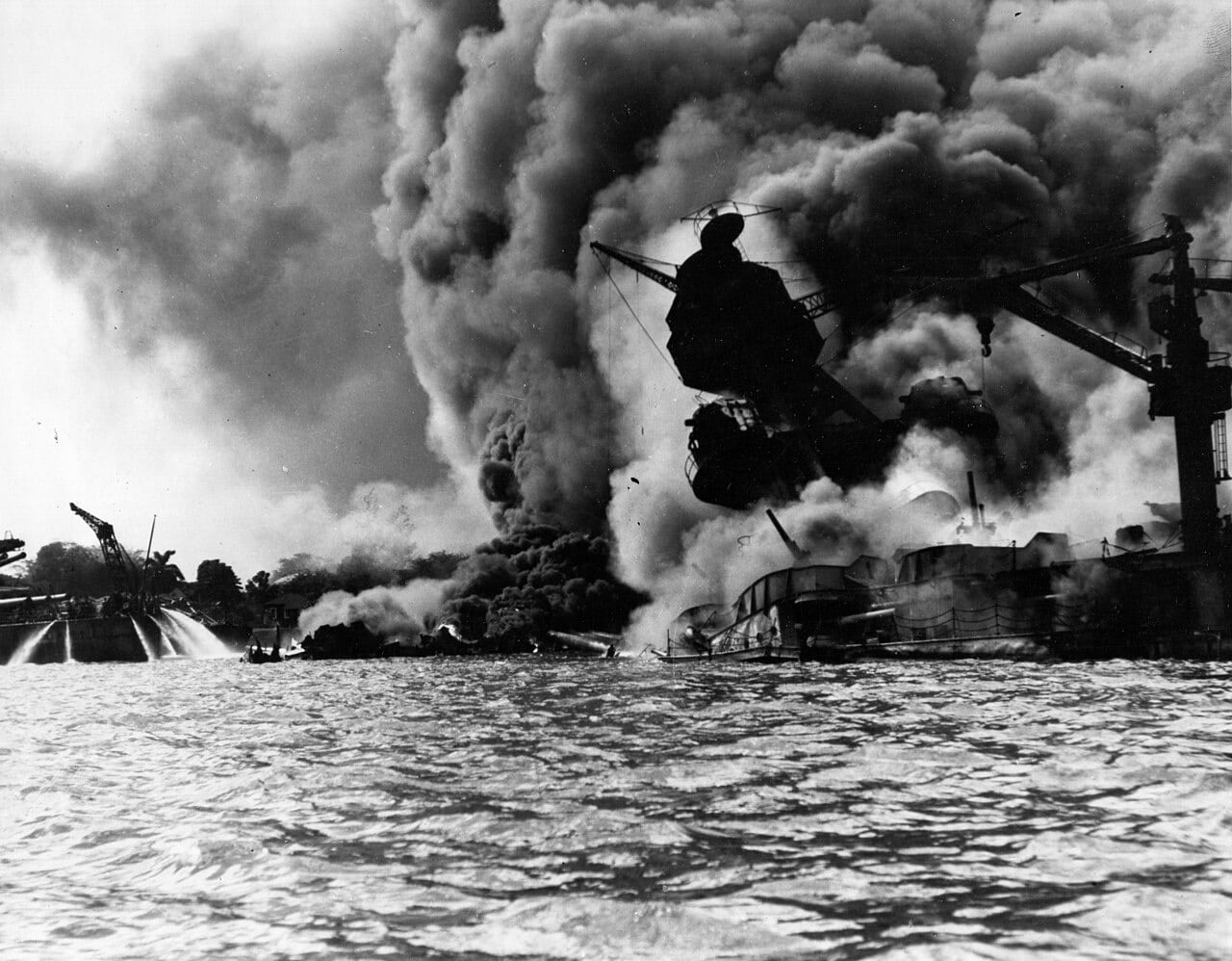 The battleship USS Arizona sunk and burning at her mooring, smoke pouring from the wreck