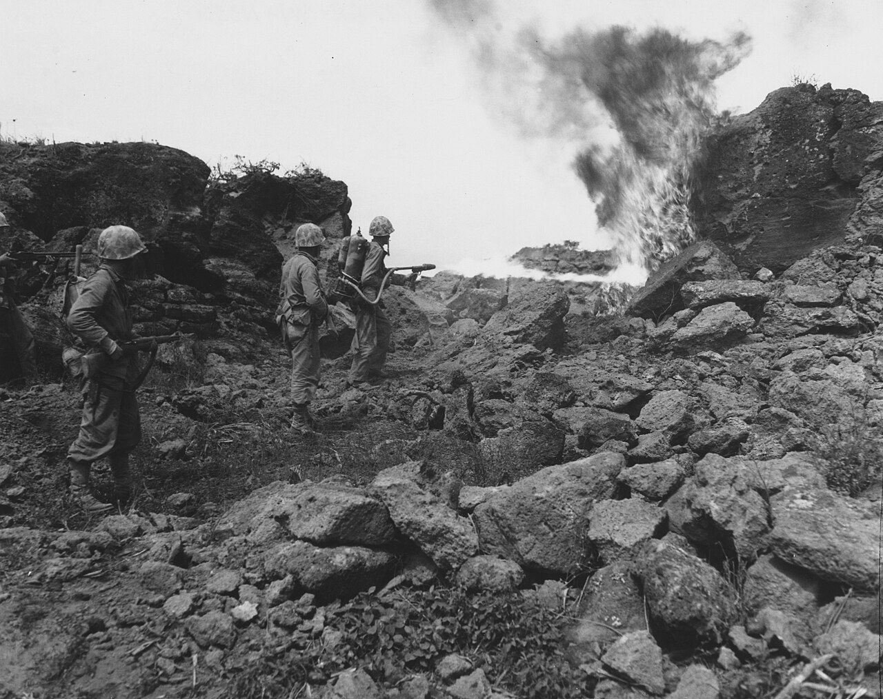 A Marine firing a portable flamethrower at a hillside position