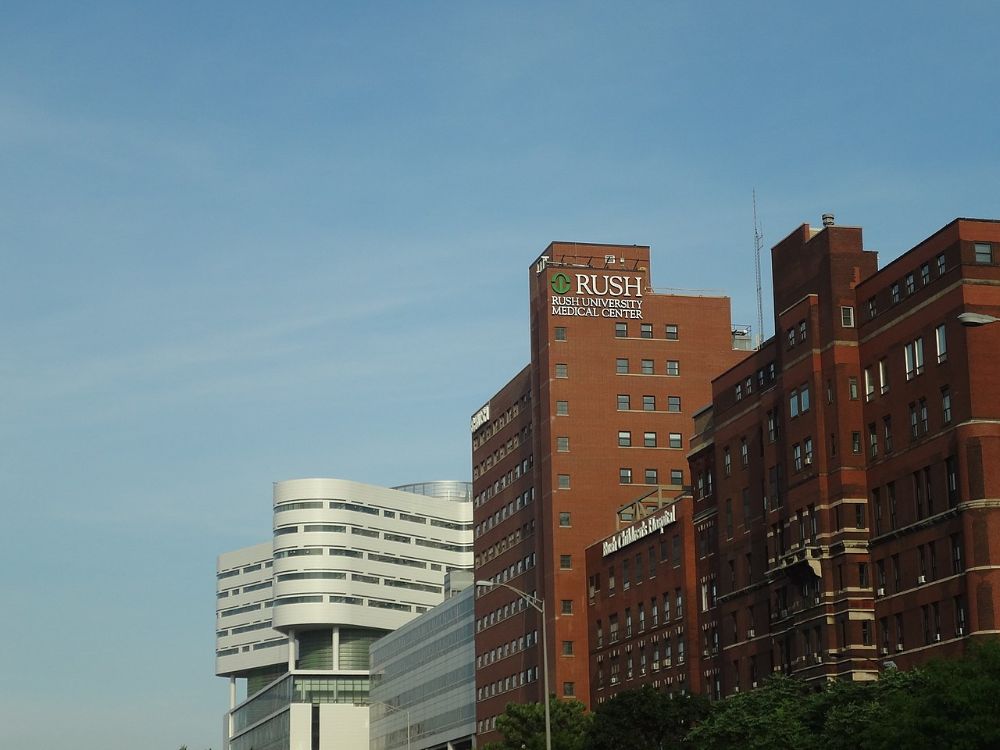 Red-brick hospital towers of Rush University Medical Center in Chicago under a blue sky, with a modern white tower to the left
