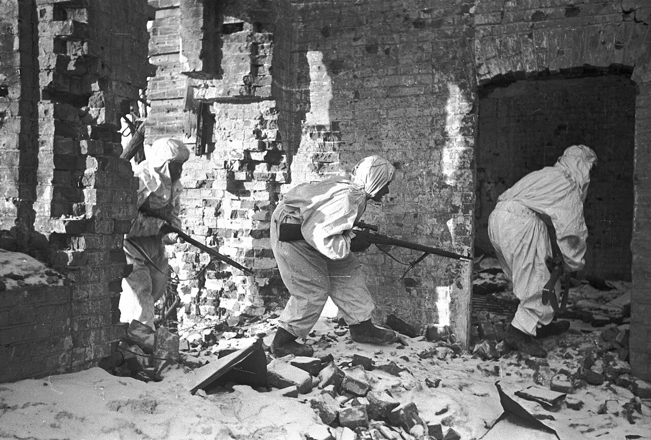 Snipers in white camouflage capes entering a ruined brick house