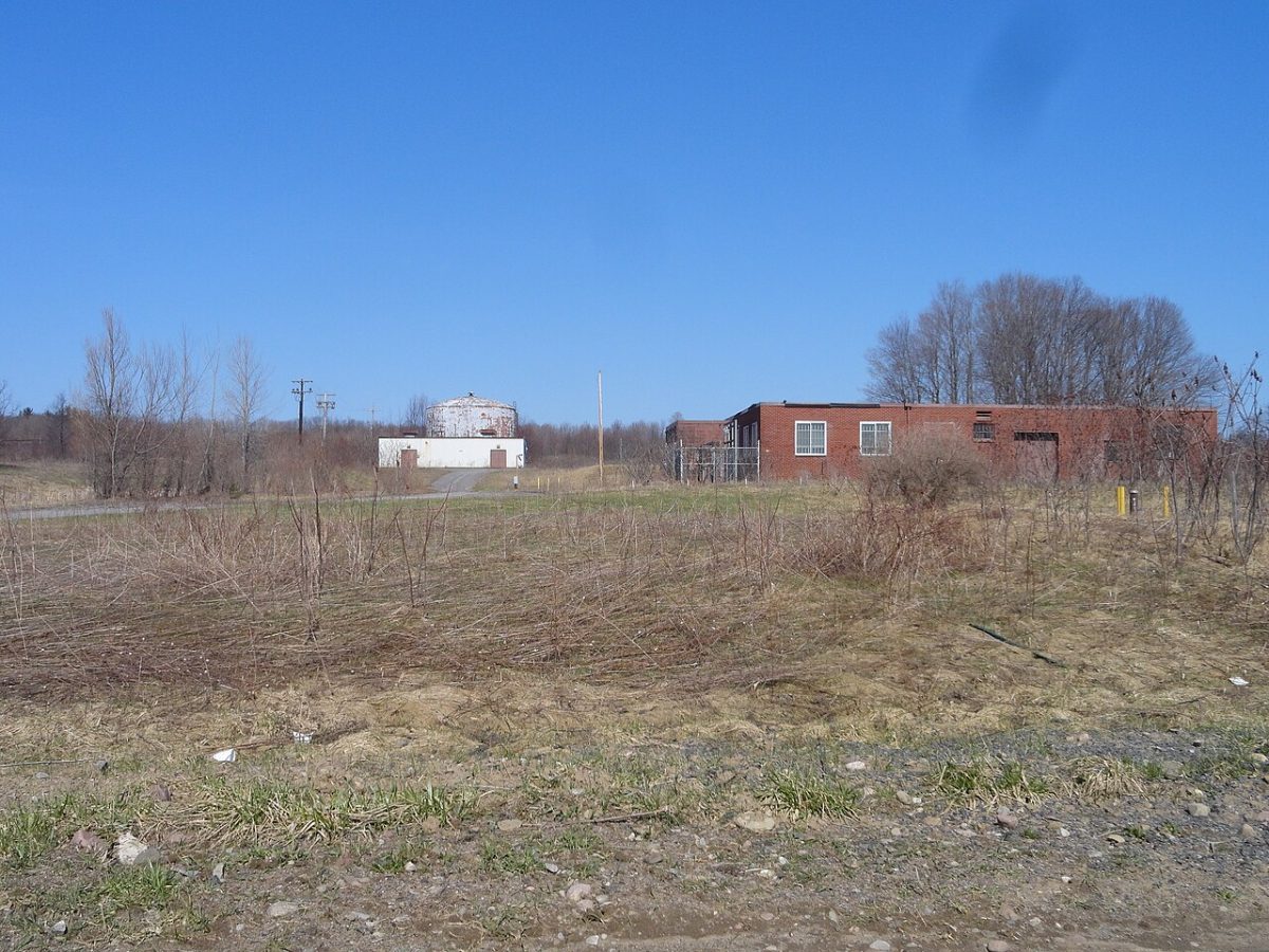 Low brick buildings and a water tower standing behind scrubby open ground at the decommissioned Griffiss Air Force Base